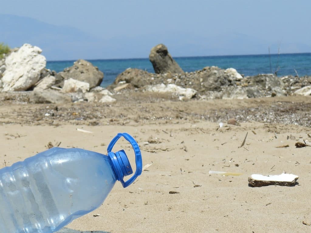 A plastic bottle sticking out of the ground with a littered beach in the background