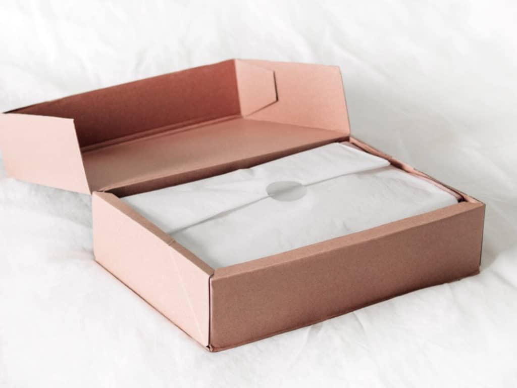 An opened pink box with an item wrapped in white tissue paper unboxing