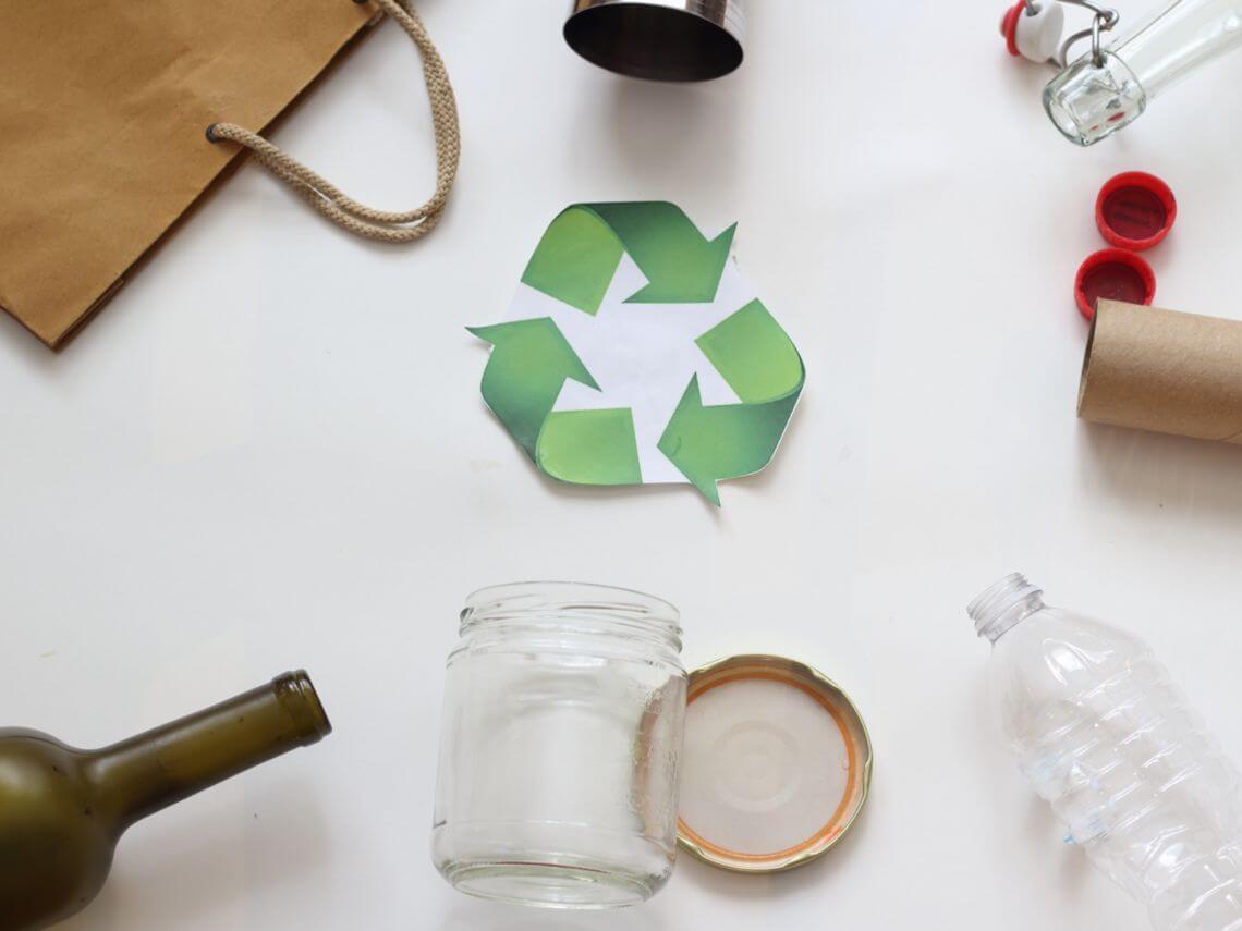 The recycle logo that is surrounded by discarded items that are recyclable