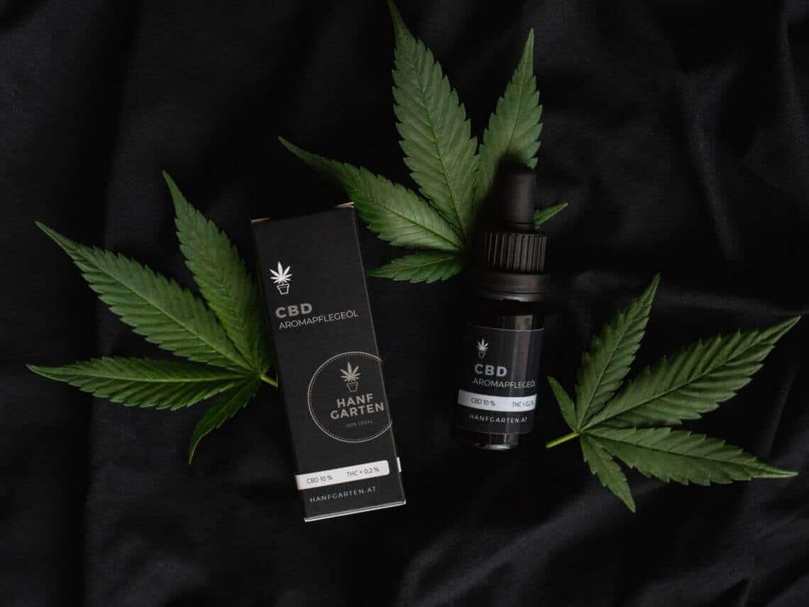 A black bottle and small box of CBD products lie on top of Cannabis leaves