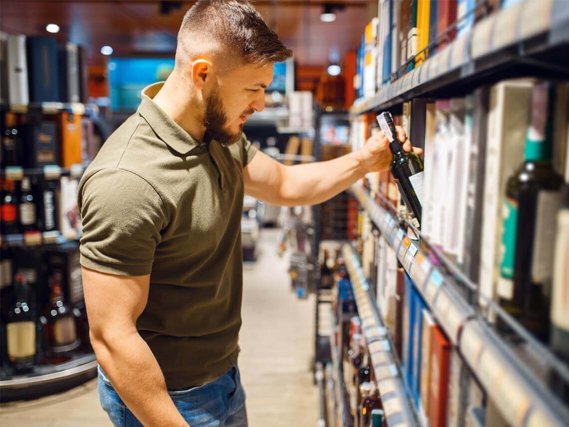 A younger man shopping for alcohol looking for a sustainable bottle