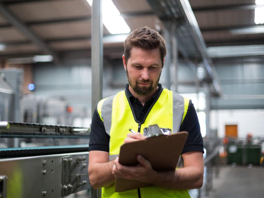 Man in warehouse looking at clipboard reviewing maintenance methods