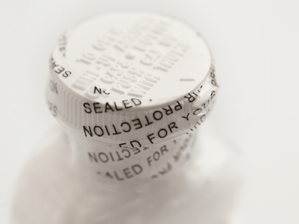 A close-up view of a white plastic bottle with a tamper-evident seal on the cap. The seal features clear, bold text indicating "SEALED FOR YOUR PROTECTION," wrapping around the cap to ensure the contents have not been tampered with.